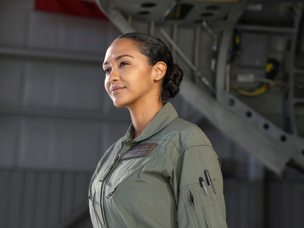 Una mujer vistiendo una camisa de trabajo verde con bolígrafos enganchados en el bolsillo de su manga en un hangar de aviones