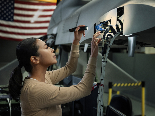 A woman holding a flashlight inspecting the internal components of an unmanned aerial vehicle