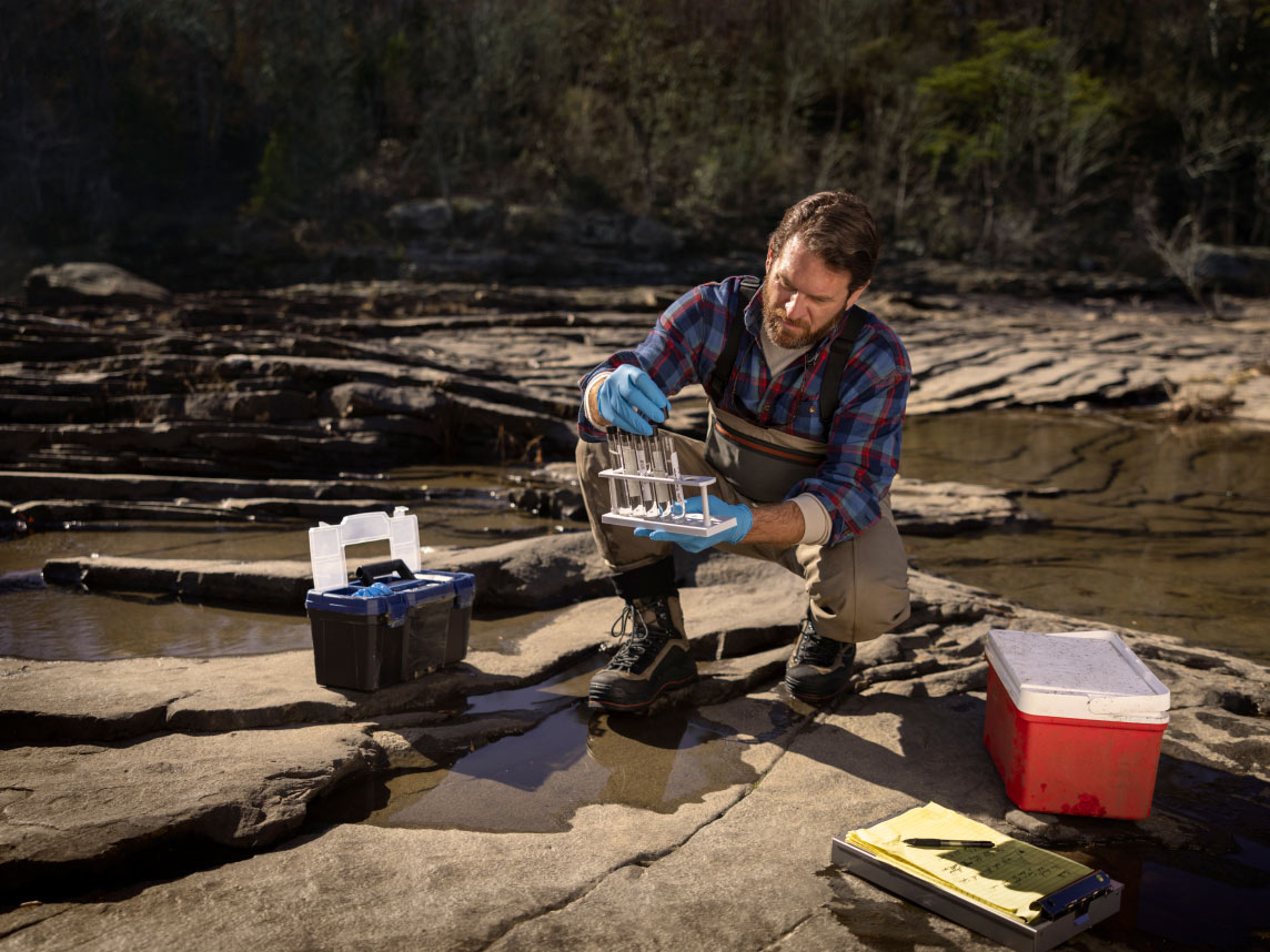 Un hombre recopilando muestras de agua de río en tubos de ensayo en una reserva forestal