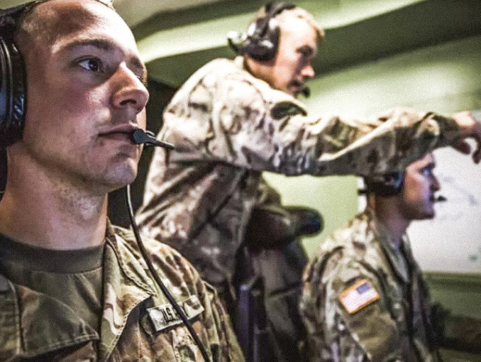 Three Army Soldiers in uniform wearing headsets looking at screens in front of them