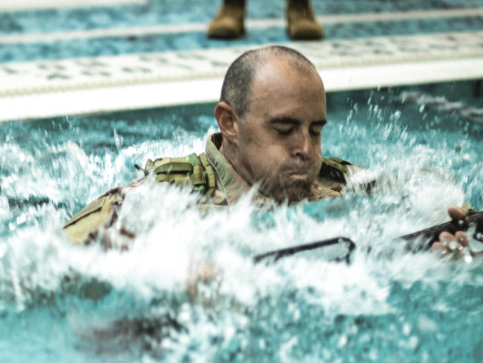 A Soldier in combat uniform training in an indoor pool 