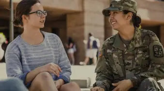 Female ROTC cadet in combat uniform having a friendly conversation with a fellow student