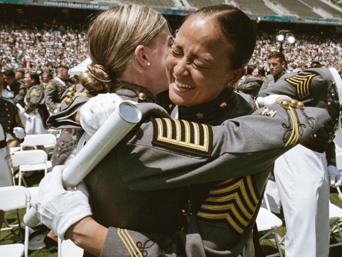 Two female West Point cadets celebrating at a large graduation ceremony