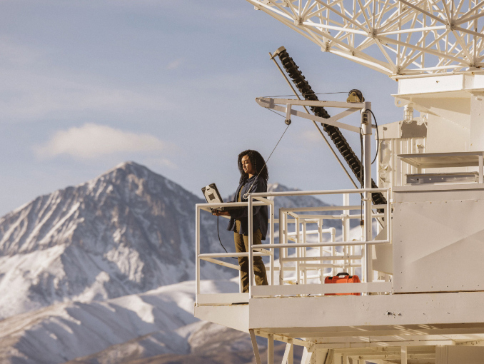 Un ingeniero Civil del Army especializado en satélites, parado en una torre de satélite trabajando en una computadora portátil