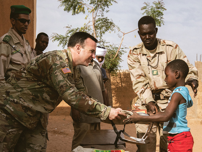 Civil Affairs Soldier smiling and interacting with a child and local civilians in a foreign community.