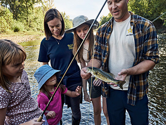A family standing in a river with a fish hooked onto a fishing rod