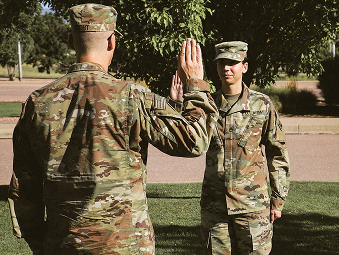 Two Soldiers in uniform standing on a lawn and facing each other with their right hands pointed upwards