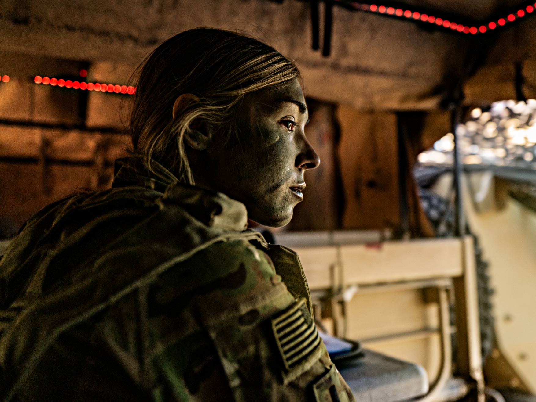 Una Soldado del Army con la cara pintada, sentada y mirando fijamente en la parte trasera de un vehículo con la cajuela abierta