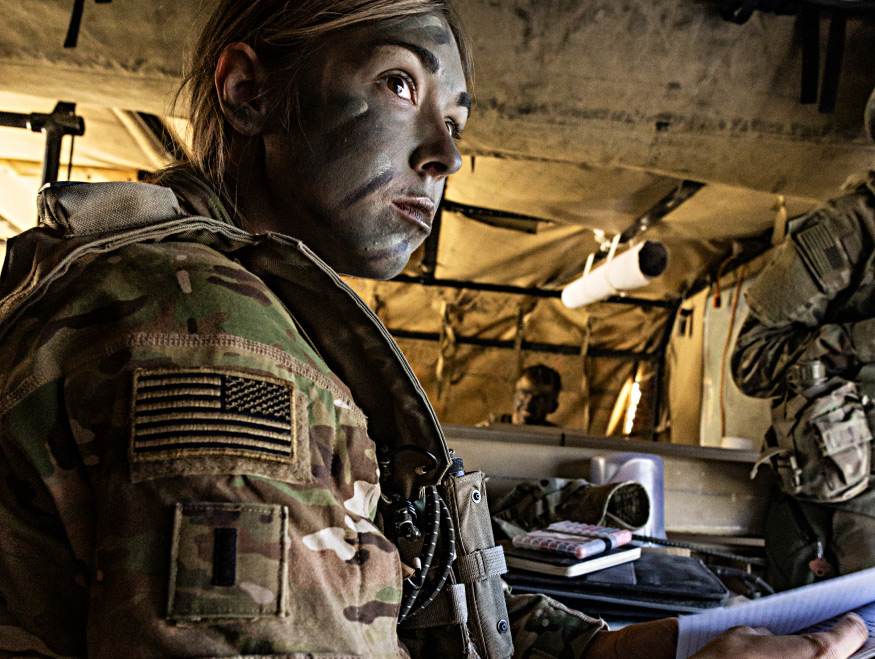 Female Soldier in uniform and facepaint sitting down while looking focused
