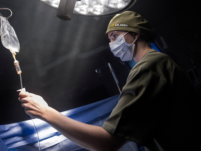 Army Medicine doctor wearing a mask and adjusting an IV in an operating room