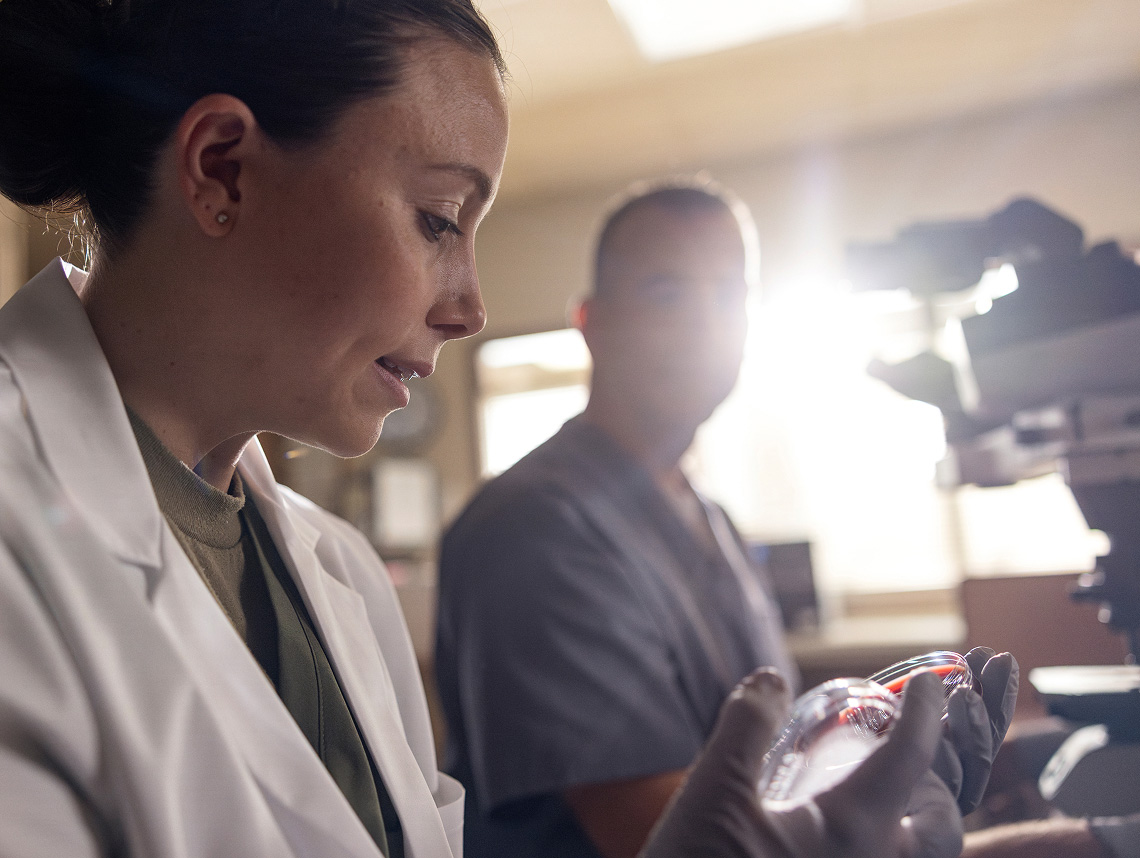 Female Army Medicine doctor in white lab coat staring at her palms with a microscope in the background