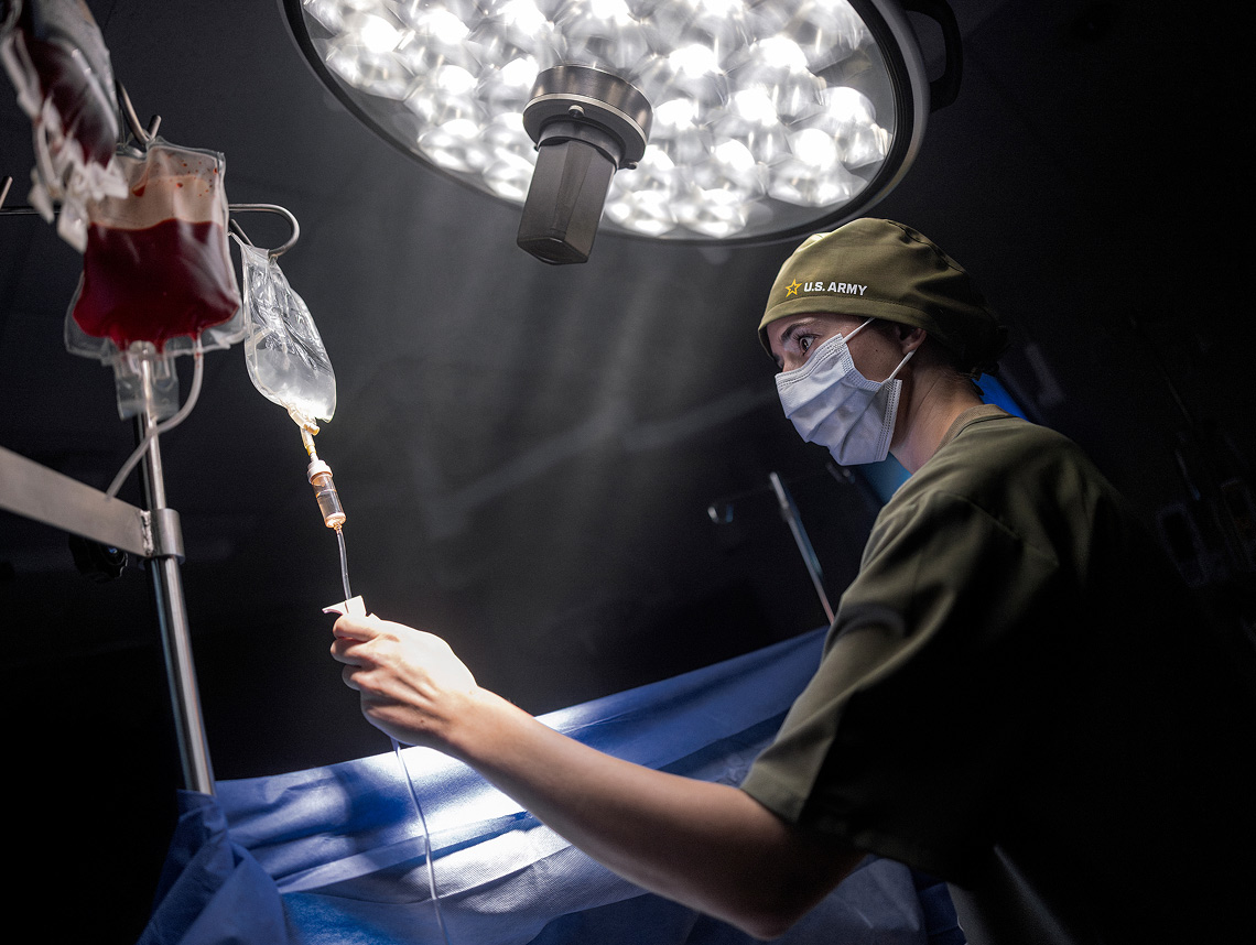 Doctora de Medicina del Army con mascarilla y ajustando el suero en un quirófano