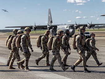 Eight Soldiers walking on an aviation runway with a jet in the background