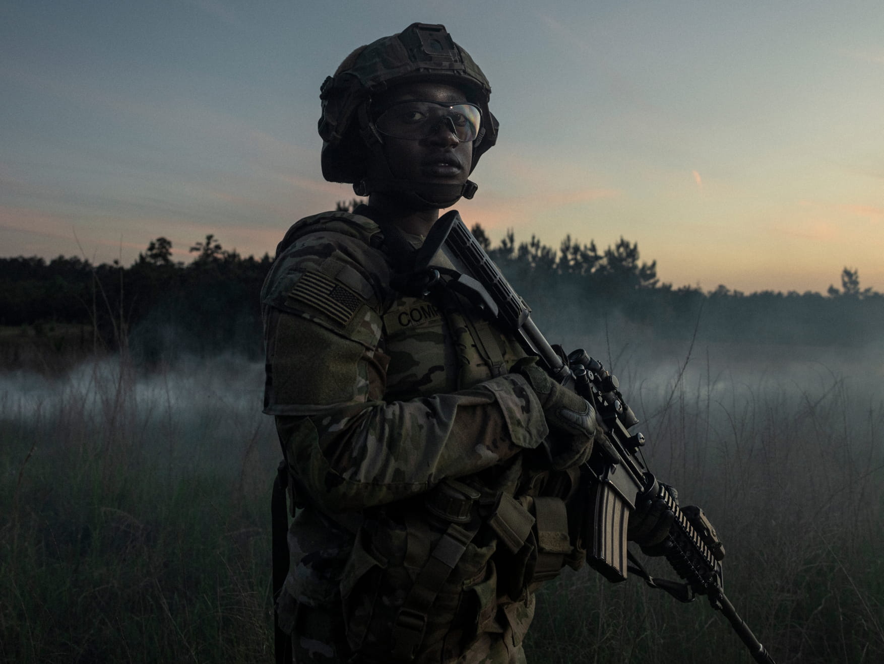 Soldier holding a rifle and standing in a field at dawn