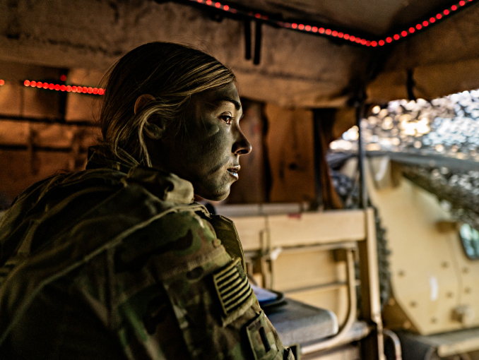 Female Army Soldier with facepaint sitting and staring intently in the back of a vehicle with its trunk open