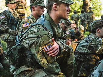Male Soldier in uniform reaching across his own body with other Soldiers surrounding him