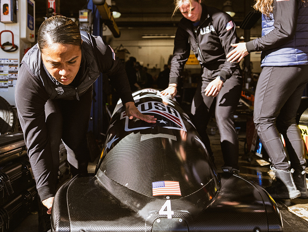 Specialist Azaria Hill with a focused expression and in a lunge position next to a bobsled