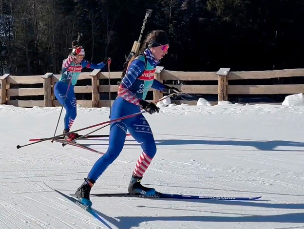 Staff Sergeant Deedra Irwin wearing a red, white, and blue biathlon uniform while cross-country skiing with ski poles in hand and rifle on back