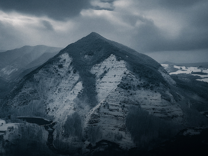 Vista aérea de una montaña blanca cubierta de árboles de hoja perenne con un cielo nublado de fondo