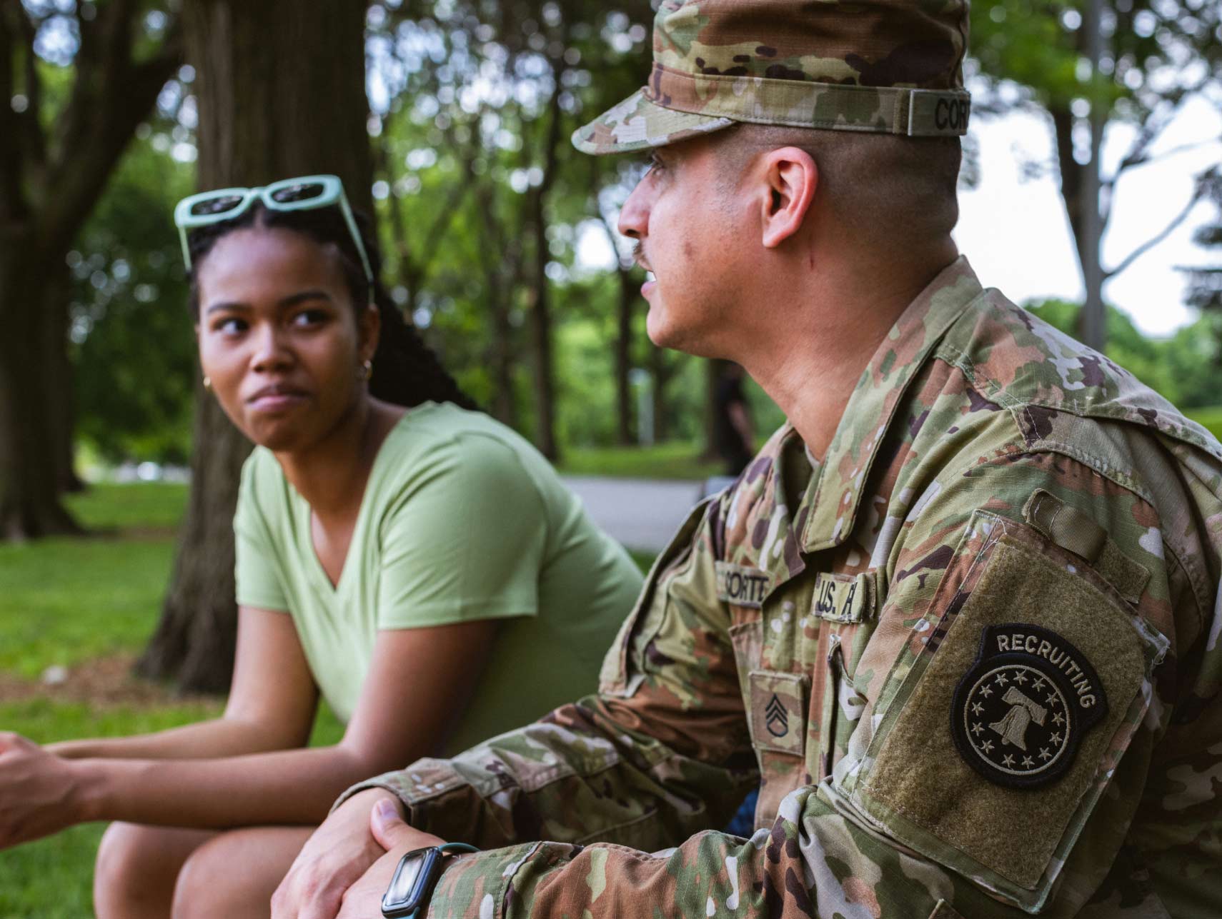 A male Army recruiter talking to a young female sitting on a bench outdoors