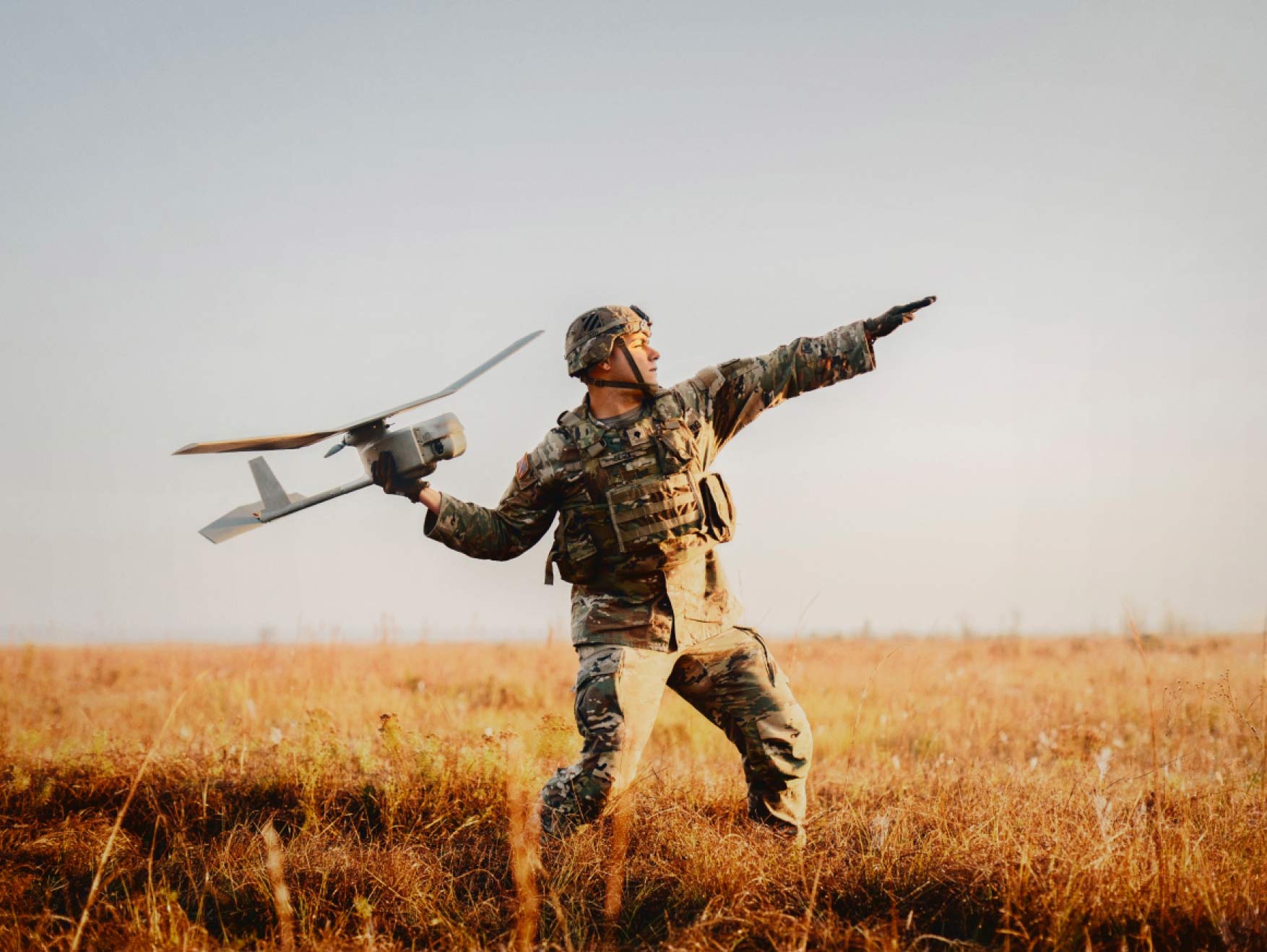 An Army Soldier in combat gear launching a drone in a field