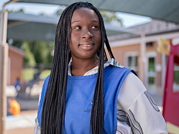 A smiling young woman looking into the distance while standing outside in front a building 