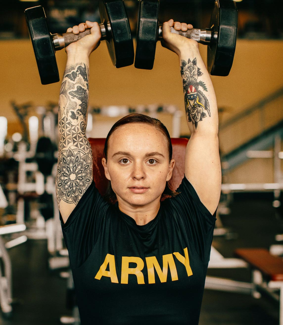 Una Soldado con una camiseta del Army levantando unas mancuernas por encima de su cabeza