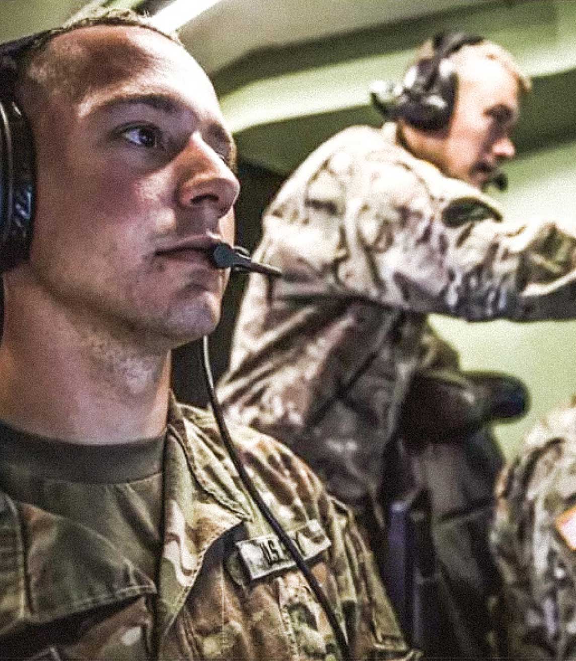 Three Army Soldiers in uniform wearing headsets looking at screens in front of them