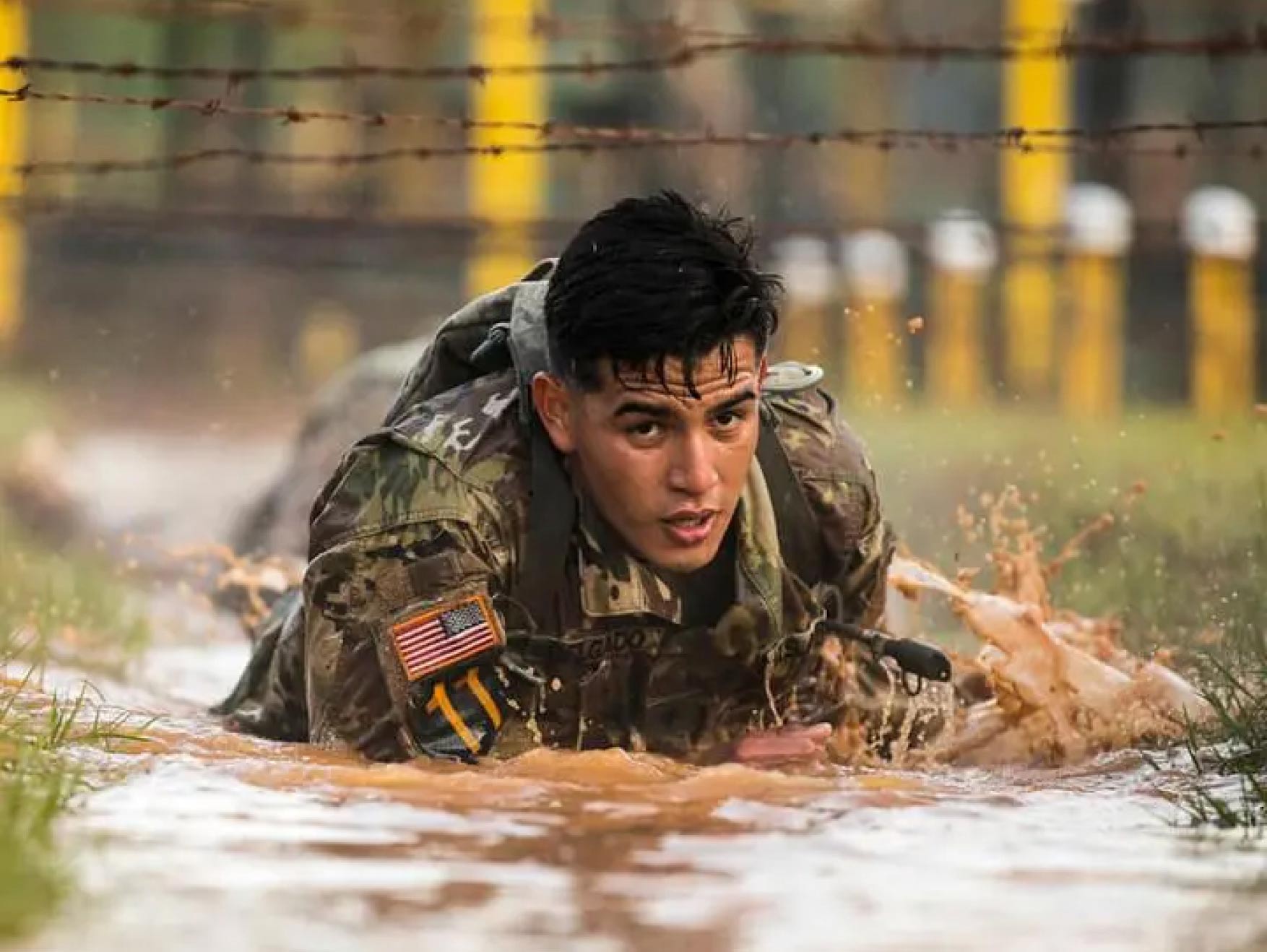 An Army Ranger crawls through the mud during an obstacle course