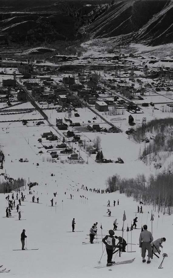 Esquiadores dispersos en la ladera de una montaña con un pueblo de esquí al fondo