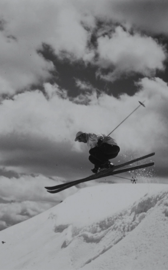 Walter Prager en el aire sobre sus esquís, con un montón de nieve debajo y un cielo nublado de fondo