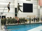 Cadets participating in combat water survival training. Each cadet must enter the water blindfolded from the high dive and then remove the blindfold and their equipment before swimming to the edge of the pool.