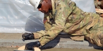 Soldier smooths a wet concrete surface .