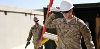Soldiers carrying a ladder and other tools to use on buildings which will be deconstructed during an engineer project.