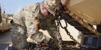 Soldier adjusting chains securing a M1A1 Abrams tank to a M1000 trailer.